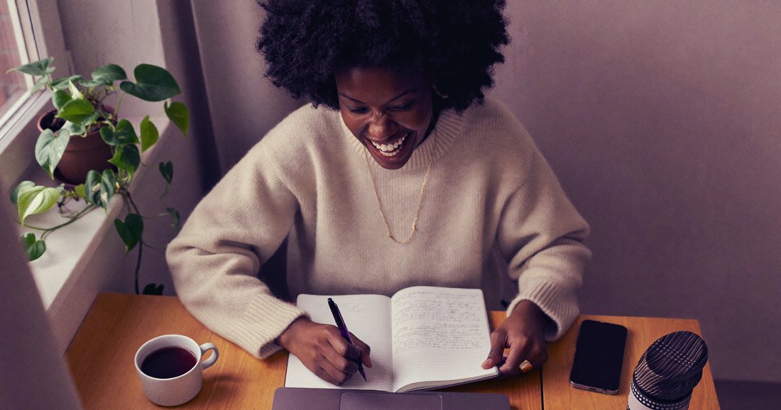 Une indépendante travaille en souriant à son bureau, carnet ouvert à côté de son ordinateur portable.